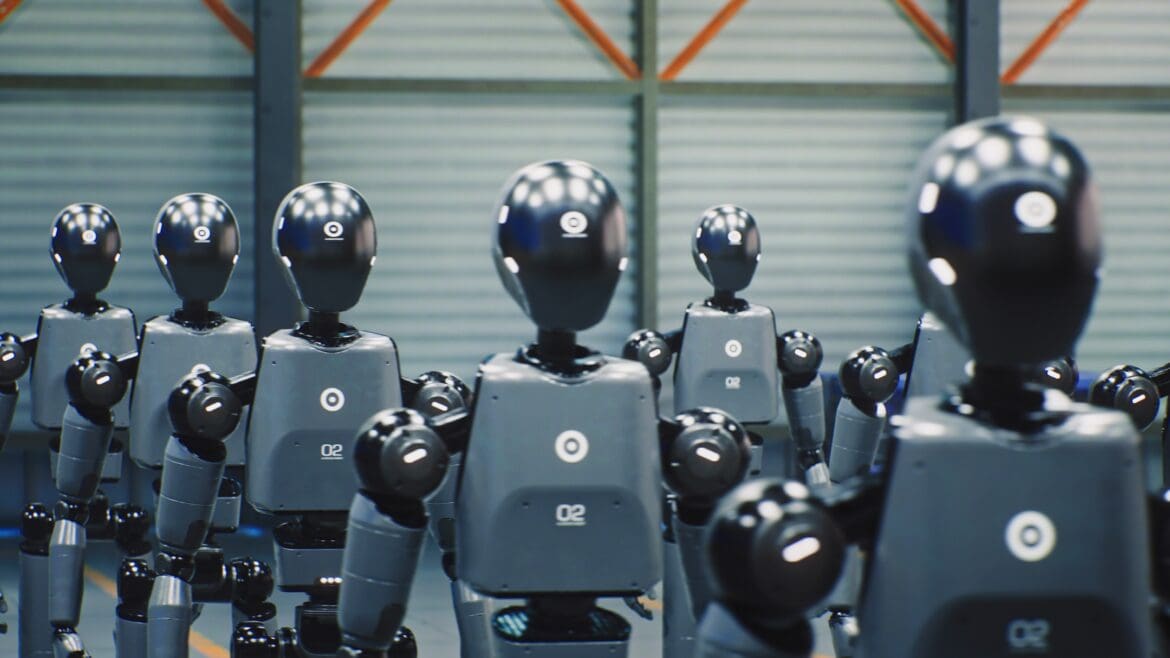 Rows of identical grey-and-black humanoid robots standing in a factory, illustrating the rise of physical AI and robotics.